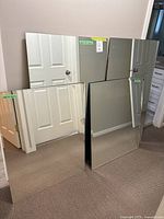 Four large rectangular mirrors leaning against walls, reflecting parts of doors and rooms. Two mirrors show bevelled edges, one or more have visible edge chipping and wear.