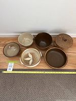 Overview of six assorted pottery bowls arranged on wood floor with a measuring tape showing sizes, different colors and designs visible
