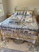 Full view of queen size brass bed with bedding and folded linens on top in a room with natural light from window