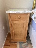Side view of the pine wood side table featuring one drawer and one cabinet door with wooden knobs.