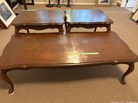 Set of two side tables and one coffee table with wood grain pattern, curved edges and visible scratches.