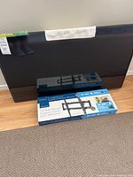 42 inch Samsung TV leaning against wall with boxed Insignia tilting wall mount on floor in front.
