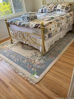 Wool area rug in bedroom setting under brass bedframe with cream, blue, and pink floral pattern visible