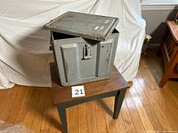 Front view of metal ammo box on table showing lid partially open