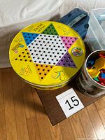 Round yellow tin with Chinese Checkers board on lid, blue plastic case beside it