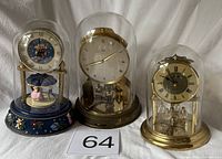 Three anniversary clocks under glass domes side by side