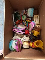 Box containing assorted paper lanterns, plastic mugs, tin noisemakers, ice cream scoop