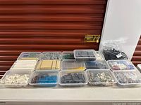 Wide view of thirteen clear tubs of assorted Lego bricks and one bag on table