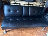 Full view of black faux leather futon sofa bed showing tufted backrest and seat, metal legs, and overall condition.