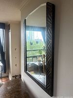 Full view of mirror showing geometric embossed metal frame with antique bronze/brown finish, mounted on wall reflecting room interior.