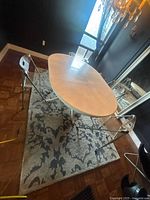 Full view of oval dining table with chairs and visible extension leaf set on a gray patterned rug in dining room