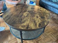 Side angle view of coffee table showing the black metal legs and metal mesh lower storage tier under the wooden top.
