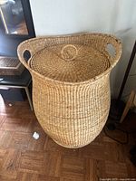 Full view of large woven basket with lid on wooden parquet floor showing basket shape and handles