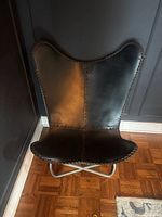 Front view of butterfly chair showing dark leather seat with hand-stitched edges and ergonomic butterfly shape.
