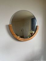 Full view of the round wall mirror mounted on a wall, showing the natural wood frame covering the bottom quarter.