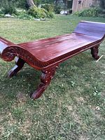 Full view of carved wood bench on lawn showing scrolled end and two legs