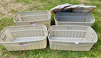 Four large Rubbermaid Roughneck totes on grass, three lids visible
