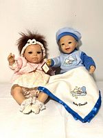Front view of both dolls seated; Rosie in pink outfit, Baby Donald in blue sleeper holding blanket, tags visible