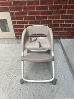 Front view of beige baby high chair showing seat, footrest and wheels