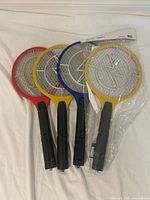 Front view of four electric bug zapper rackets, colors red, yellow, blue, sealed yellow unit