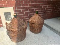 Front view of both wicker-encased demijohns showing size difference and handles