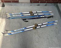 Two pairs Splitkein skis with four poles laid out on ground