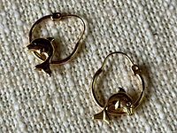 Pair of small 10kt gold hoop earrings with dolphin charms on a textured white surface.