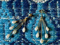 Pair of 14K yellow gold earrings with dangly freshwater pearls displayed on a blue patterned fabric.