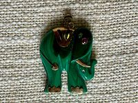 Photo of the carved malachite elephant pendant with gold accents on a fabric background.