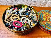 Top-down view of the antique tin filled with buttons and buckles showing the contents clearly.