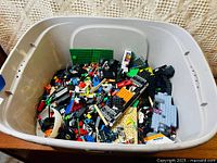 Large plastic tub filled with assorted mixed LEGO pieces from a variety of sets.