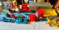 Collection of vintage toys on a table including a battery operated monkey, tin toy motorcycle, wooden BRIO dump truck and airplane, large plastic rig truck, small plastic cars.