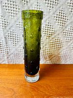 Front view of a tall olive green bubble glass vase with clear base on wooden surface against textile background