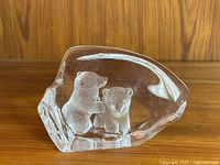 Clear lead crystal paperweight showing two engraved polar bear cubs inside, placed on wooden surface.