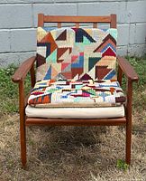 Front view of teak armchair with seat and back cushions against concrete block wall