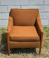 Front view of the mid-century modern armchair showing rust-orange upholstery and teak front arm panels.
