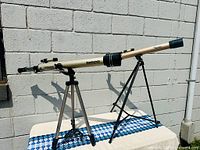 Full view of refractor telescope mounted on aluminum tripod against a white wall