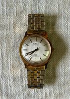 Full view of gold-tone men's Timex automatic wristwatch with link bracelet on textured white background.