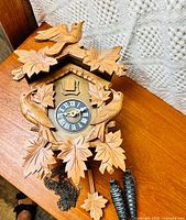 Front view of vintage Blackforest cuckoo clock with carved birds and leaves, hanging pinecone weights, and clock face