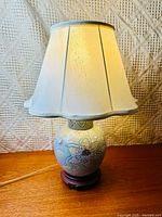 Front view of the lamp with fabric shade, showing the cream color and scalloped edge of the shade, wooden table surface below.