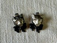 Pair of vintage panther cat head clip-on earrings with black bows on a beige fabric background.