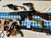 Top-down view of entire collection showing all toy guns and leather holsters laid out on patterned cloth