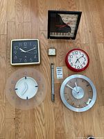 Front view of all six clocks and thermometer on wood floor