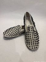 Pair of white leather loafers with black spikes, three-quarter view