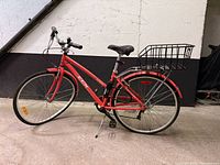 Full view of coral CCM Lucerne bicycle with basket and bent front wheel