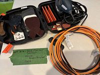 Open case showing Mouse sander, sanding accessories, coiled extension cord
