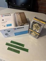 Moen Caldwell faucet kit box beside Defiant deadbolt lock box