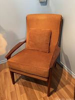 Front view of teak armchair with orange upholstery and cushion