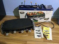 Grill set laid out with box, pans, forks, manuals and power cord visible