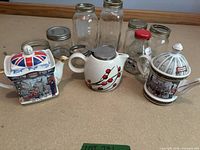 Front view of three teapots and seven jars/bottles on tabletop